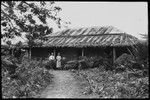 European man and woman, with female native in front of house