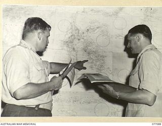LAE, NEW GUINEA. 1944-11-26. QX6188 CAPTAIN G.A.G. DEAR, STAFF LEARNER (1) AND VX45390 CAPTAIN D.K. THORNTON (2) CHECKING UP THE LATEST SITUATION IN THE AREA ON A LARGE WALL MAP IN THE OPERATIONS ..