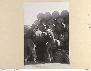 AITAPE BEACH HEAD, NEW GUINEA. 1945-06-19. SAPPER H.C. GAMMON (1) AND SAPPER E.A. ANDERSON (2), MEMBERS OF 7 DOCKS OPERATING COMPANY, ROYAL AUSTRALIAN ENGINEERS, STACKING DRUMS OF FUEL ON BOARD A ..