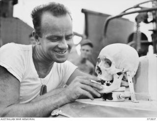 ALEXISHAFEN, NEW GUINEA. 1944-04-30. LIEUTENANT (JUNIOR GRADE) E. V. MCPHERSON, OF COLUMBUS, OHIO WITH A JAPANESE SKULL WHICH SERVES AS A MASCOT ABOARD THE UNITED STATES NAVY MOTOR TORPEDO BOAT 341