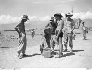 MALAHANG BEACH, LAE, NEW GUINEA. 1945-10-16. TROOPS OF FIRST ARMY WHO HAVE BEEN UNLOADING AMMUNITION BOXES PAUSE FOR A MUG OF COLD FRUIT JUICE. SURPLUS AMMUNITION IS BEING DESTROYED AT MALAHANG ..