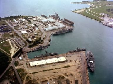 An aerial view of various ships moored in the harbor at the US Naval Ship Repair Facility