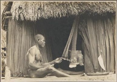 Mailu Island types [man seated outside a hut making a net] Frank Hurley