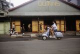 French Polynesia, woman driving scooter past Quinn's nightclub in Papeete