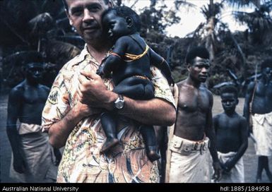European man holding baby, Papua New Guinean behind him