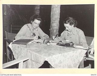 PALMALMAL PLANTATION, JACQUINOT BAY, NEW BRITAIN. 1945-07-22. PRIVATE J. STILLMAN (1) AND PRIVATE R. GARTHON (2), MEMBERS OF THE AUSTRALIAN ARMY MEDICAL WOMEN'S SERVICE SPENDING THE EVENING WRITING ..