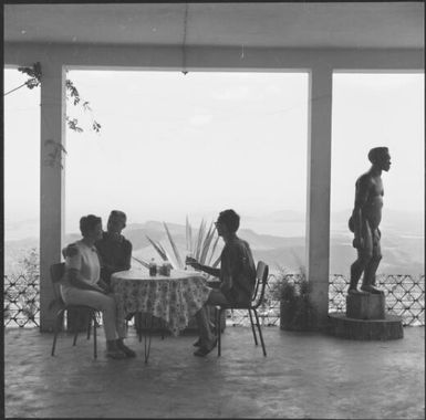 Three people sitting on verandah over looking Mont Koghi, New Caledonia, 1967 / Michael Terry