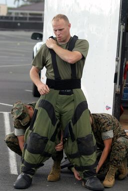 U.S. Marine Corps SGT. Maya and SGT. Garcia, Headquarters Battalion, assist SGT. Pretz (standing), Explosive Ordnance Disposal SPECIALIST, Combat Service Support Group-3, into a bomb suit at the Marine Corps Base Hawaii, Hawaii, Post Exchange parking lot on Dec. 9, 2004.(U.S. Marine Corps official photo by CPL. Nicholas Riddle) (Released)