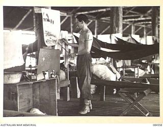 LABU, NEW GUINEA. 1944-12-22. SAPPER D. GORDON, ARTIST AND EDITOR OF BARGING ON, THE UNIT'S UNOFFICIAL ORGAN, AT WORK ON HIS CHRISTMAS POSTERS. HIS MAGAZINE RECEIVED AN EXCELLENT REVIEW IN "SMITH'S ..