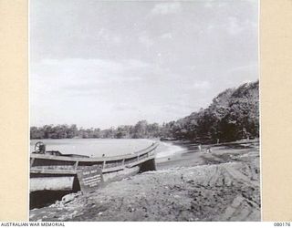 SCARLET BEACH, NEW GUINEA. 1944-07-04. AN ABANDONED JAPANESE INVASION BARGE. AUSTRALIAN SERVICEMEN RE-CUPERATE IN THE BACKGROUND. NOTE THE DESCRIPTIVE TABLET PROPPED AGAINST THE BARGE