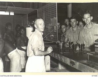 LAE SX39708 PRIVATE R. JOHNSTON, ASSISTED BY NATIVES FROM THE AUSTRALIAN NEW GUINEA ADMINISTRATIVE UNIT, SERVING SOFT DRINKS TO SERVICE PERSONNEL AT THE 22ND ARMY CANTEEN SERVICES OTHER RANKS CLUB ..