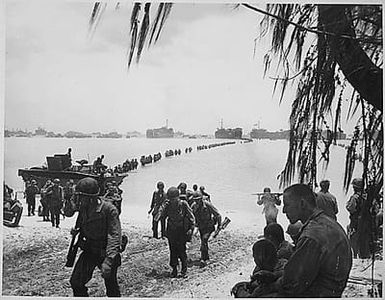 Army reinforcements disembarking from LST's form a graceful curve as they proceed across coral reef toward the beach. Saipan.