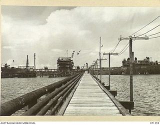 PORT MORESBY, PAPUA, 1944-03-21. THE PATHWAY ALONG THE WHARF LEADS TO THE OIL TANKER EMPIRE SILVER WHICH IS BERTHED IN THE DISTANCE. THE OIL LINES RUNNING ALONGSIDE THE WHARF LEAD TO BULK OIL ..