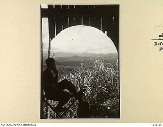 ALEXISHAFEN, NEW GUINEA, 1944-05-18. NX120677 CORPORAL R. MALONE (1), 35TH INFANTRY BATTALION, ADMIRING THE VIEW FROM THE VERANDAH OF YELBECK MISSION, AN OLD CATHOLIC MISSION SITUATED NORTH OF ..