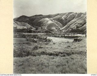 WAU - LAE ROAD, NEW GUINEA, 1944-02-26. THE WATUT RIVER PICTURED WITH THE SUNSHINE MINE ON THE LEFT AND THE SCAR CUT BY THE ROAD AROUND THE MOUNTAINS ON THE RIGHT. THE ROAD FROM SUNSHINE CAMP ..