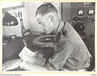 WEWAK, NEW GUINEA. 1945-10-29. SERGEANT N.S. BRAY, 1 BROADCASTING STATION, AUSTRALIAN ARMY AMENITIES SERVICE AT THE MICROPHONE OF RADIO STATION 9AJ DURING A BROADCAST