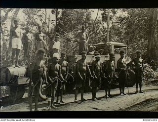 Finschhafen, New Guinea. 1944. Indigenous (native) Papuans stand in front of a truck carrying knapsack sprays which carry a special oil, used to spray mosquito breeding places. The men work for the ..