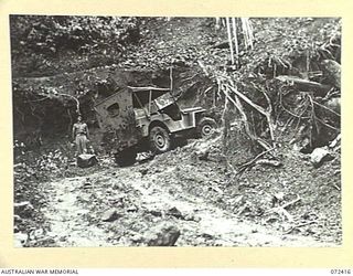 DUMPU AREA, NEW GUINEA, 1944-04-18. CORPORAL HARRIS, 15TH FIELD COMPANY, ROYAL AUSTRALIAN ENGINEERS BESIDE THE JEEP ON A SHARP CORNER DURING STEEP ASCENT OF THE ROAD