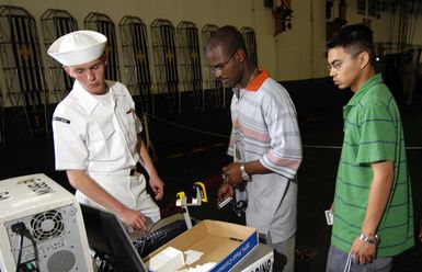 US Navy (USN) Aviation Electronics Technician Third Class (AT3) Jonathan White (left) monitors USN Sailors scanning their military identification cards before leaving for liberty using an electronic scanner onboard the USN USS KITTY HAWK (CV 63). All Sailors stationed aboard the carrier are required to check in and out using a bar code scanner