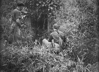 BOUGAINVILLE ISLAND. 1945-01-18. Q33451 PRIVATE V.M. PERROUX (1) AND QX35765 LIEUTENANT A.E.C. MULLALY (2) INSPECTING A JAPANESE PILLBOX WHICH APPEARS TO HAVE BEEN USED AS AN AMMUNITION STORE