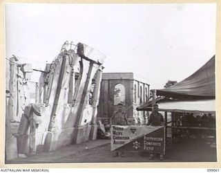 RABAUL, NEW BRITAIN. 1945-11-20. PRIVATE E. NIBLETT (1) AND PRIVATE F.W. HOLMES (2), STANDING AT THE YOUNG MEN'S CHRISTIAN ASSOCIATION - AUSTRALIAN COMFORTS FUND, 5 BASE HUT, WHICH HAS BEEN ERECTED ..