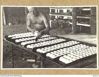 DUMPU, RAMU VALLEY, NEW GUINEA. 1943-11-24. NX136757 PRIVATE C. BINDON OF WALLSEND, NSW, A BAKER OF THE 4TH AUSTRALIAN FIELD BAKERY GLAZING BREAD ROLLS PRIOR TO BAKING