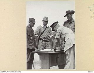 CAPE WOM, NEW GUINEA, 1945-09-13. MAJ-GEN H.C.H. ROBERTSON, GOC 6 DIVISION, SIGNING THE INSTRUMENT OF SURRENDER. LT-GEN H. ADACHI, COMD 18 JAPANESE ARMY IN NEW GUINEA, FORMALLY SURRENDERED TO ..