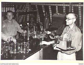LAE, NEW GUINEA. 1945-11-25. SERGEANT WAPPET SERVING DRINKS AND PRIVATE G. TAPPER LOADING HIS TRAY IN THE BAR OF THE AUSTRALIAN ARMY CANTEENS SERVICE OFFICERS' CLUB. THE CLUB IS SITUATED ON THE ..