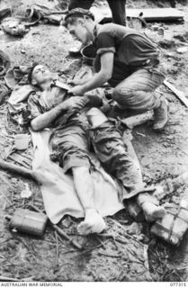 TOROKINA AREA, BOUGAINVILLE ISLAND. 1944-11-29. PRIVATE J. J. RYAN (LEFT) WOUNDED DURING THE ATTACK BY D COMPANY, 9TH INFANTRY BATTALION, ON LITTLE GEORGE HILL, RECEIVING MEDICAL ATTENTION FOR HIS ..