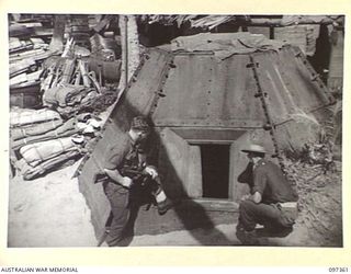 BUIN AREA, BOUGAINVILLE. 1945-09-28. DRIVER J. SEYMOUR (1) AND LIEUTENANT C.E. ATKINS (2), OF 9TH INFANTRY BATTALION, INSPECTING A STEEL PILLBOX, ONE OF MANY FORTIFIED POSITIONS THAT LINE THE COAST ..