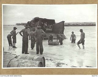 SIALUM, NEW GUINEA. 1944-01-05. PERSONNEL OF "D" COMPANY, 2/3RD AUSTRALIAN PIONEER BATTALION UNLOADING 44 GALLON DRUMS OF PETROL FROM AN LCM (LANDING CRAFT, MECHANISED) ON TO THE BEACH