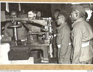 LITHGOW, NSW. 1944-01-25. AUSTRALIAN AND NEW GUINEA ADMINISTRATION UNIT NATIVES WATCHING MR J. J. WRAY (EXAMINER) TESTING A .303 LEE ENFIELD RIFLE FOR CORRECT SIGHTING AT THE SMALL ARMS FACTORY