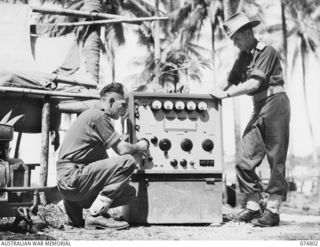 MILILAT, NEW GUINEA. 1944-07-16. LANCE CORPORAL W.J. MITCHELL (1) AND QX40794 MAJOR F. SCOTT (2) OF HEADQUARTERS SIGNALS, 5TH DIVISION, EXAMINING A MODEL 94, TYPE 2, 300 WATT, RADIO TRANSMITTER ..