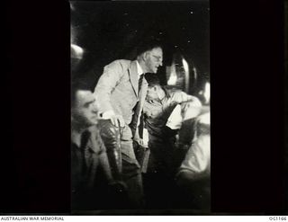 IN FLIGHT BETWEEN HOLLANDIA, DUTCH NEW GUINEA AND AITAPE, NORTH EAST NEW GUINEA. C. 1944-06. ARTHUR DRAKEFORD (STANDING), THE MINISTER FOR AIR, LOOKING THROUGH THE WINDOW OF THE AIRCRAFT DURING THE ..