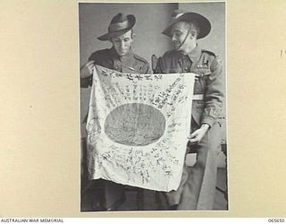 MELBOURNE, VIC. 1944-04-19. A JAPANESE FLAG CAPTURED BY MEMBERS OF THE 2/12TH INFANTRY BATTALION AT FINSCHHAFEN ON THE 2ND OCTOBER, 1943, DISPLAYED BY GUNNER PARKER, LEFT (1) AND GUNNER TOWNSEN (2)