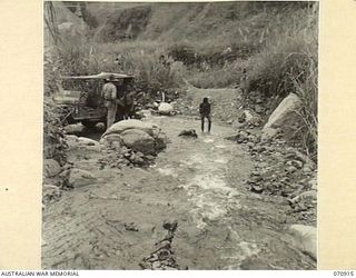 WAU - LAE ROAD, NEW GUINEA, 1944-02-26. NX8309 SAPPER C.J. THOMPSON (1), OF THE 1ST MECHANICAL EQUIPMENT PLATOON, 2/1ST RAILWAY CONSTRUCTION COMPANY, (MECHANICAL EQUIPMENT), PAUSES AT A FORD ON THE ..