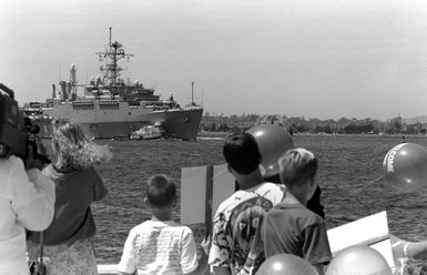 A crowd watches from the pier as a commercial harbor tug escorts the miscellaneous flagship USS CORONADO (AGF-11), flagship for commander, Third Fleet, toward a pier at Naval Station, North Island. The CORONADO has arrived at its new home port after spending almost 20 years in Hawaii