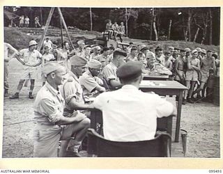 JACQUINOT BAY, NEW BRITAIN, 1945-08-23. OFFICIALS, STEWARDS AND BROADCASTER AT THE ROYAL NEW ZEALAND AIR FORCE VICTORY CUP RACE MEETING. OFFICERS ARE THROWING DICE TO CONTROL THE MOVEMENT OF WOODEN ..