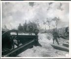 WWII, a Japanese sugar refinery in ruins, Infantrymen pass the ruins of a demolished sugar refinery. Blasted by bombs and naval gunfire. One curious gaze and they are off after the desperately fighting "Nips" (Japanese), Saipan, The Mariana Islands