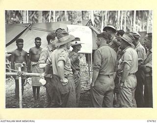 MILILAT, NEW GUINEA. 1944. TROOPS OF HEADQUARTERS, 5TH DIVISION STUDYING THE DETAILS OF THE COMMONWEALTH REFERENDUM FROM THE NOTICES ON THE UNIT EDUCATION OFFICE NOTICE BOARD