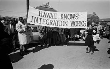 Charles M. Campbell and Nona Ferdon holding a banner reading, ""Hawaii Knows Integration Works," in the George Washington Carver Homes neighborhood of Selma, Alabama, before the Selma to Montgomery March.