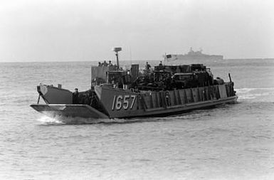 The utility landing craft LCU-1657 begins to lower its ramp as it approaches the beach at Vieques, Puerto Rico, during Fleet Ex 1-90. In the background is the amphibious assault ship USS SAIPAN (LHA-2)