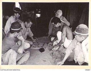 VUNAPOPE, NEW BRITAIN. 1945-09-16. JAPANESE NAVAL GUARDS SQUATTING ON THE FLOOR OF THEIR TENT PLAYING A GAME RESEMBLING DRAUGHTS. FOLLOWING THE SURRENDER OF THE JAPANESE.  AUSTRALIAN TROOPS NOW ..