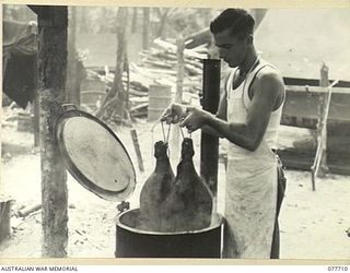 BOUGAINVILLE ISLAND. 1944-12-24. NX35312 PRIVATE W.F. STAMP, COOK, 9TH INFANTRY BATTALION PLACING CHRISTMAS HAMS IN A COPPER FOR THE UNIT CHRISTMAS DINNER
