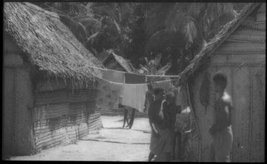 Houses with man and a woman holding a baby : Carteret Islands, Papua New Guinea, 1960 / Terence and Margaret Spencer