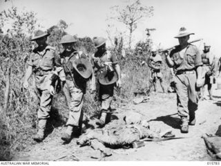 1943-09-22. NEW GUINEA. AUSTRALIAN TROOPS CAPTURE LAE. AUSTRALIAN TROOPS FILE PAST A DEAD JAPANESE ON THEIR WAY INTO LAE