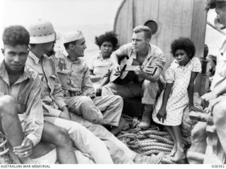 NEW GUINEA, 1942-08-03. THREE AMERICAN SOLDIERS AND A MANDOLIN AMUSING A COUPLE OF NATIVES DURING A RIVER VOYAGE IN NEW GUINEA
