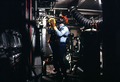 A member of a firefighting team inspects machinery during a drill aboard the amphibious assault ship USS GUAM (LPH 9)