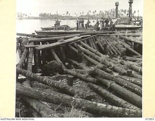 MADANG, NEW GUINEA. 1944-04-24. AUSTRALIAN TROOPS EXAMINE THE PIER WHICH HAS BEEN BOMBED BY THE RAAF. MOORED AT THE BACKGROUND ARE MOTOR TORPEDO BOATS OF THE UNITED STATES NAVY