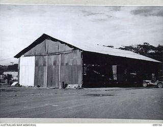 LAE, NEW GUINEA, 1945-11-26. THIS BUILDING, FORMERLY USED BY GUINEA AIRWAYS, IS NEAR THE AERODROME. ITS HEAVY STEEL FRAME SAVED IT FROM EXTENSIVE DAMAGE. IT HOUSES THE MOBILE OVERHEAD HOIST. THE ..